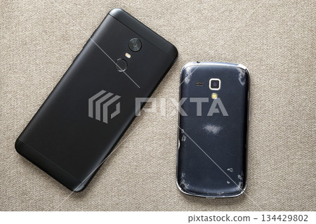 Comparison of two black mobile phones, old cellphone and new modern on light cloth copy space background. Technology progress and replacement concept. 134429802