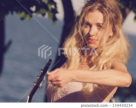 Woman playing acoustic guitar in park Woman playing acoustic guitar in park 134430234
