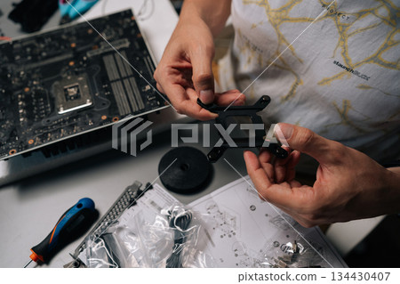 Computer technician mounting CPU cooler bracket on motherboard, ensuring precise hardware installation during computer system maintenance. Concept of computer hardware, repairing, upgrade. Computer technician mounting CPU cooler bracket on motherboard, ensuring precise hardware installation during computer system maintenance. Concept of computer hardware, repairing, upgrade. 134430407