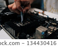 Close-up of technician hand meticulously applying thermal paste to CPU of computer motherboard, demonstrating process of computer maintenance and repair. Concept of computer hardware, repairing 134430416
