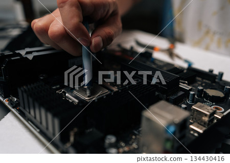 Close-up of technician hand meticulously applying thermal paste to CPU of computer motherboard, demonstrating process of computer maintenance and repair. Concept of computer hardware, repairing 134430416
