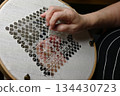 hands carefully stitching a delicate geometric lace pattern on white linen stretched in an embroidery hoop 134430723