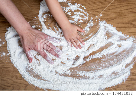 Adult and Child Hands Spreading Flour on Wooden Kitchen Surface 134431032