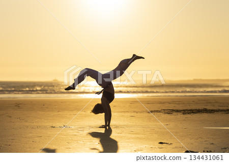 Person performing capoeira handstand on beach at sunset Person performing capoeira handstand on beach at sunset 134431061