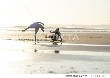 People performing capoeira movements on sandy beach at sunset 134431062