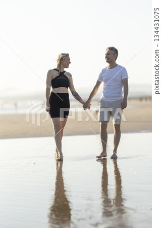 Romantic couple walking on beach holding hands at sunset Romantic couple walking on beach holding hands at sunset 134431075