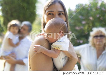 Mother holding newborn baby bonding with family outdoors 134431115