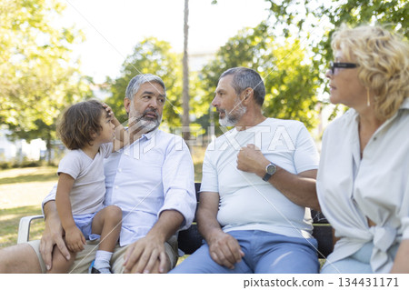 Grandparents and grandchild having conversation sitting on park bench 134431171