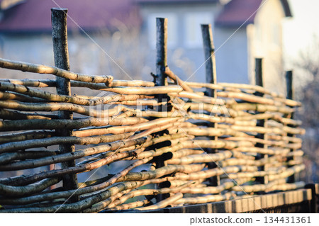 A rustic wicker fence made of wooden branches glowing in the warm golden sunlight of a peaceful garden A rustic wicker fence made of wooden branches glowing in the warm golden sunlight of a peaceful garden 134431361