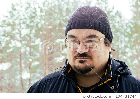 Large stern man with mustache and neat beard close up against snowy winter forest background. 134431744