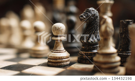 antique wooden chess pieces pawn, knight on a checkered board. The focus is on the frontline pieces, symbolizing strategy, battle, business planning, intellectual rivalry, logic, and classic games 134432198