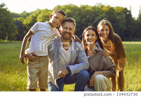 Portrait of happy family with son and daughter sitting in the summer park and looking at camera. 134432730