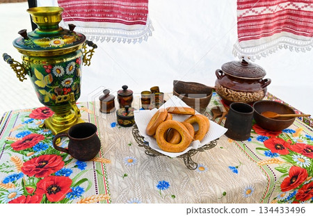 Traditional Slavic tea setting with painted samovar, poppy tablecloth, bagels, and clay dishes. Russian folk culture and colorful patterns. Traditional Slavic tea setting with painted samovar, poppy tablecloth, bagels, and clay dishes. Russian folk culture and colorful patterns. 134433496