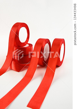 Bright satin ribbons in a vivid red hue arranged in rolls on a clean background. Smooth decorative material ideal for floral design craft gift wrapping and festive projects. Bright satin ribbons in a vivid red hue arranged in rolls on a clean background. Smooth decorative material ideal for floral design craft gift wrapping and festive projects. 134433498