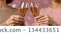 Two women toasting with champagne glasses against a festive pink background with bokeh 134433651
