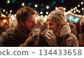 Couple enjoying warm drinks at festive outdoor market with twinkling lights and cozy atmosphere 134433658