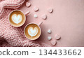 Two cups of heart-shaped latte art on pink background with cozy knitted blanket and candies 134433662