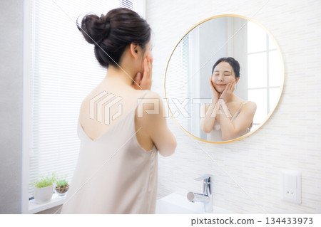 Young woman looking in the mirror in the bathroom 134433973