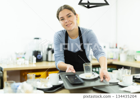 Young female waitress collects dirty dishes 134435204