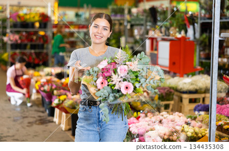 Young woman customer holding bouquet of flowers in open-air plants market 134435308