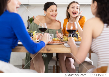 Happy women congregated around a festive table; participating in animated discussions and enjoying the delights of wine Happy women congregated around a festive table; participating in animated discussions and enjoying the delights of wine 134435313