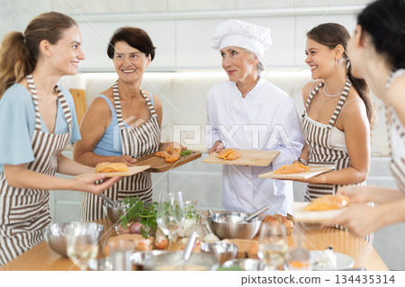 Elderly woman chef teaches group of people how to cook chicken 134435314