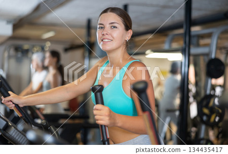Slender athletic girl during cardio exercises on elliptical simulator in fitness center. Slender athletic girl during cardio exercises on elliptical simulator in fitness center. 134435417