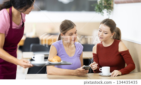 Girl waiter in apron presents coffee and croissants to restaurants guests. Girl waiter in apron presents coffee and croissants to restaurants guests. 134435435
