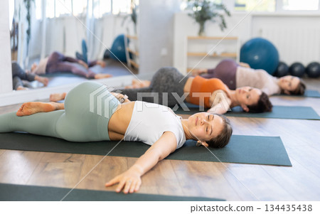 Girl teacher lead lesson, run training in female yoga studio and performs Supta Ardha Matsyendrasana 134435438