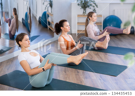 Young woman balancing in boat pose Navasana during group yoga training Young woman balancing in boat pose Navasana during group yoga training 134435453