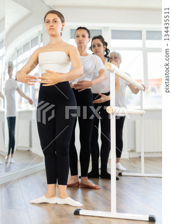 Group of women stand in position at ballet barre 134435511