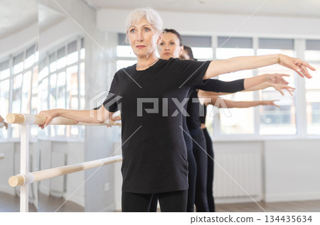 Women engaging in ballet at ballet barre in fourth position in training hall during workout session Women engaging in ballet at ballet barre in fourth position in training hall during workout session 134435634