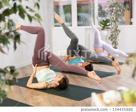 Active fit women making exersice for stress relief and practicing Plow Pose, Halasana in group yoga training on mats 134435880