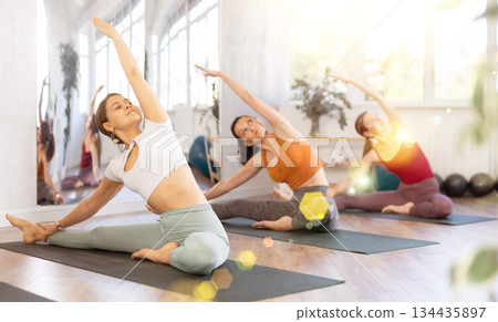 Young woman teacher perform Parivritta Janu Shirshasanawith girls in yoga studio. 134435897