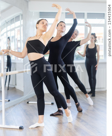 Female ballet dancers doing various ballet movements at ballet barre in fifth position Female ballet dancers doing various ballet movements at ballet barre in fifth position 134435904
