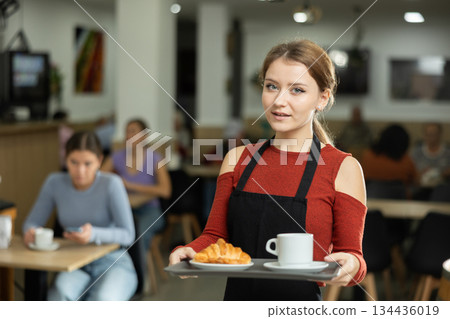 Polite waitress holding tray with coffee and croissant in cafeteria Polite waitress holding tray with coffee and croissant in cafeteria 134436019