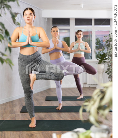 Diligent women practicing tree pose of yoga in light fitness room 134436072