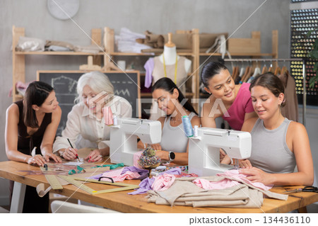 Sewing teacher helping female student with machine threading in workshop Sewing teacher helping female student with machine threading in workshop 134436110