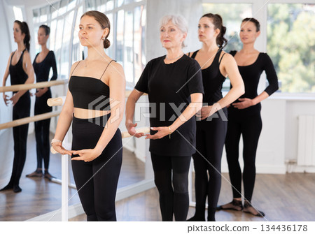Graceful women doing ballet on ballet barre in training room during training, standing in fifth position near ballet barre Graceful women doing ballet on ballet barre in training room during training, standing in fifth position near ballet barre 134436178