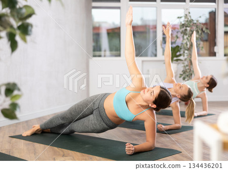 Young female yoga instructor showing others side plank in wellness center Young female yoga instructor showing others side plank in wellness center 134436201