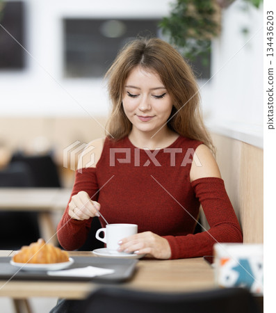 Young female sitting alone at table in cozy cafe, drinking fragrant coffee Young female sitting alone at table in cozy cafe, drinking fragrant coffee 134436203