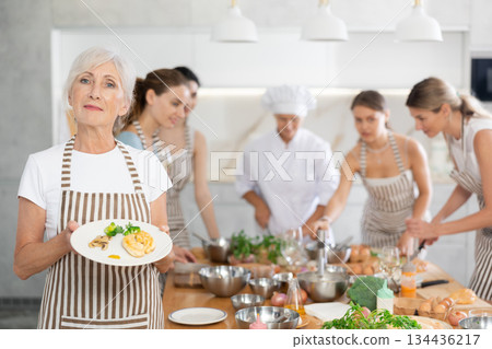Elderly woman posing with prepared chicken dish 134436217