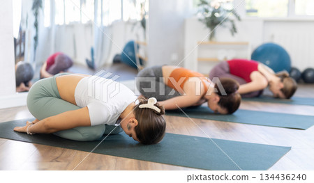 Girl teacher conducts lesson, training for girls in yoga studio and performs child pose 134436240