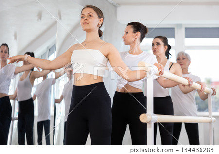 Young girl mastering second position at barre in ballet studio Young girl mastering second position at barre in ballet studio 134436283