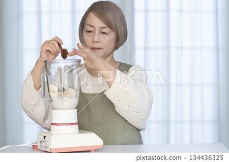 Senior woman making healthy juice with a juicer in the kitchen 134436325