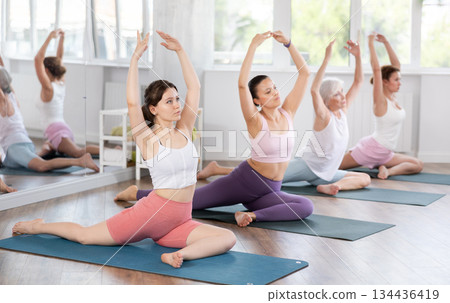 Women practicing in yoga class, focusing on flexibility and relaxation in calm studio setting 134436419