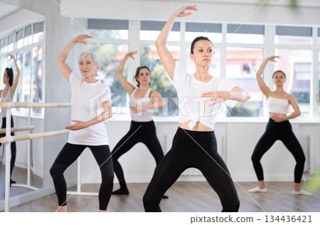Group of slender women of different ages are learning various dance and ballet movements in studio Group of slender women of different ages are learning various dance and ballet movements in studio 134436421