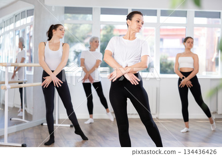 Graceful women of different ages practice various ballet movements in choreographic studio 134436426