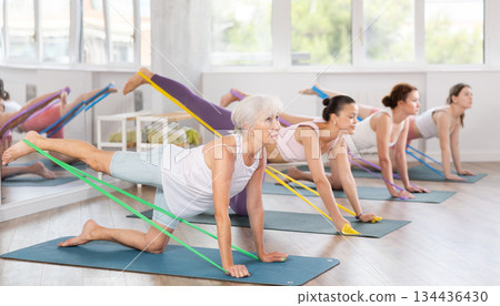 Senior lady performing exercises with resistance band in pilates class 134436430