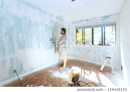 Man works on wall repair in empty room during day Man works on wall repair in empty room during day 134438155